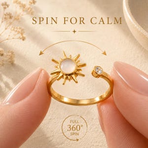May include: A gold-toned open ring featuring a sun-shaped charm with a central white stone and a small clear crystal on the opposite end. The text SPIN FOR CALM and FULL 360° SPIN is visible, indicating the sun charm rotates around the ring band.