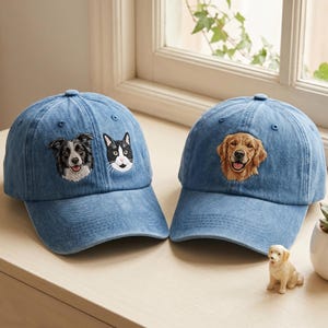 May include: Two blue denim baseball caps featuring embroidered animal portraits. The left cap displays a black and white dog and a black and white cat. The right cap features a golden-colored dog. Both caps have a structured crown and a curved brim.