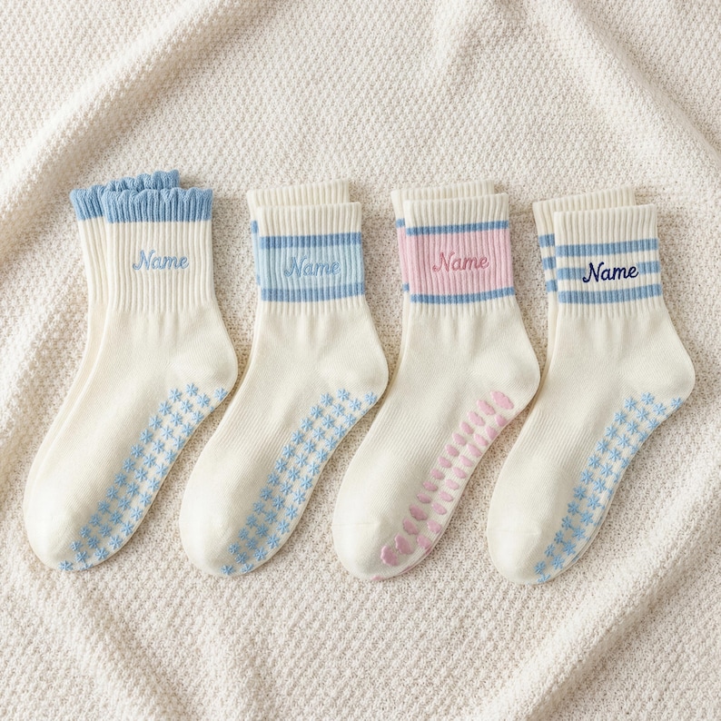 May include: Four pairs of white socks with blue or pink accents. Each sock has the word "Name" embroidered on the cuff. The socks have a floral pattern on the soles and stripes on the cuffs. The cuffs are blue or pink.