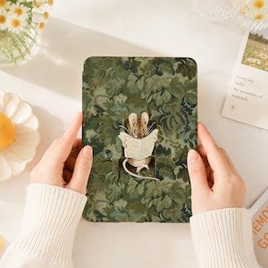 May include: A rectangular e-reader case featuring a dark green botanical pattern of leaves and foliage. Centered on the case is an illustration of a small brown mouse sitting in a dark chair while reading an open newspaper with its tail curled.