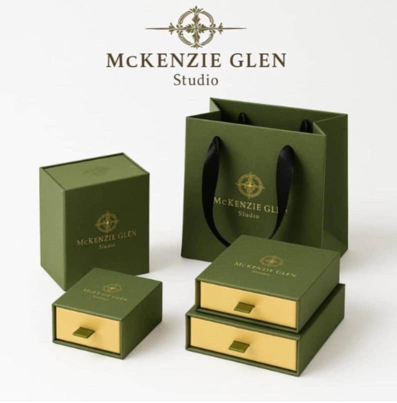 Green packaging items from McKenzie Glen Studio including square boxes, drawer boxes with gold pulls, and a gift bag with black ribbon handles.