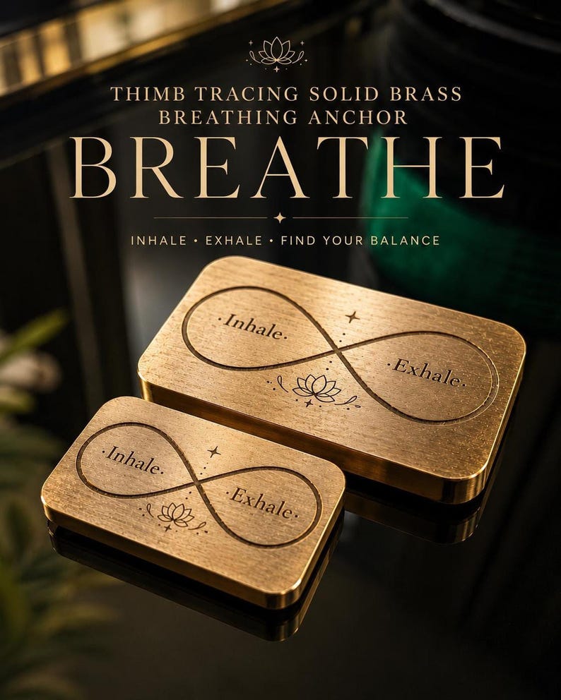 Two rectangular solid brass breathing anchors with engraved infinity symbols and the words inhale and exhale are displayed on a dark reflective surface.