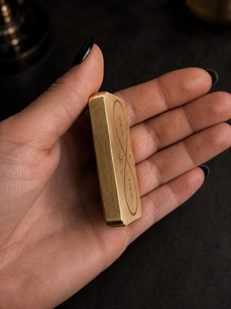 A hand holds the side profile of a rectangular solid brass breathing anchor token.
