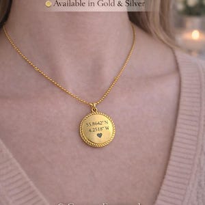 Puede incluir: Collar dorado con colgante redondo. El colgante tiene coordenadas grabadas, un símbolo de corazón y un borde en forma de cuerda. El texto "Personalised Coordinates Necklace" está en la parte superior. Disponible en oro y plata.