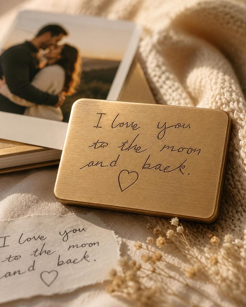 An engraved solid brass plaque with the words I love you to the moon and back rests on a knitted fabric surface next to a framed photo of a couple and a handwritten paper note.