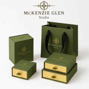 Packaging options from McKenzie Glen Studio featuring matching green and gold gift boxes, drawer boxes, and a green shopping bag with black ribbon handles.