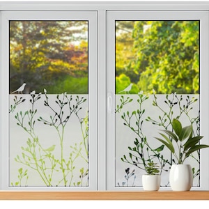 Puede incluir: Una ventana blanca con un diseño de vidrio esmerilado con ramas verdes y negras y pequeños pájaros blancos. La ventana está enmarcada en blanco con un alféizar de madera, y dos pequeñas plantas en macetas blancas están en el alféizar.
