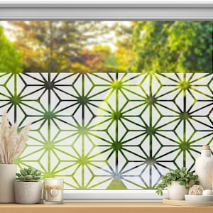 May include: A window film featuring a repeating geometric pattern of white lines on a translucent frosted background. The design consists of interconnected star-like shapes with triangular segments, applied to a window pane with a view of green trees.