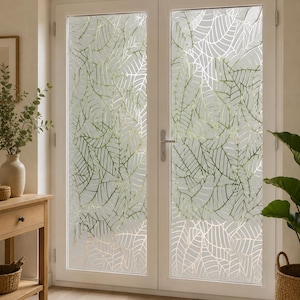 Peut inclure: Une double porte vitrée équipée d'un film d'intimité dépoli avec un motif répétitif de contours de feuilles superposés en blanc et vert clair. La porte possède un cadre blanc et une poignée en métal argenté, offrant une occultation partielle.