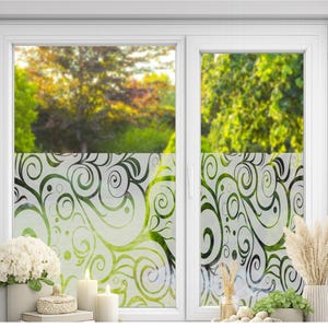 May include: A white window frame featuring a translucent privacy film with a repeating dark green and black swirling vine pattern. The film covers the lower portion of the glass panes, obscuring the view while allowing light to pass through the design.