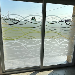 Peut inclure: Une porte-fenêtre coulissante dotée d'un film adhésif dépoli décoratif avec un motif de lignes ondulées horizontales superposées en blanc et vert clair, créant un écran d'intimité semi-transparent qui laisse passer la lumière à travers le verre.