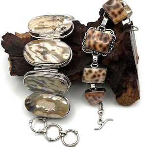 May include: Two silver bracelets. The left bracelet features four oval-shaped iridescent shell links connected by hinges. The right bracelet consists of four square and triangular-shaped tan shell links with dark brown spots, connected by silver links.