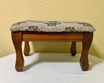 Taburete rectangular vintage con patas de madera curvadas, pátina de madera cálida.