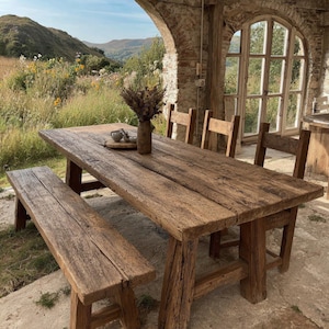 May include: A rectangular wooden dining table with a weathered brown finish, accompanied by a matching long bench and three chairs. The table surface features visible wood grain and texture, with a small ceramic vase holding dried flowers.