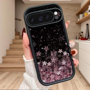 Peut inclure: Coque de téléphone noire avec un motif floral. L'étui présente un bord noir et un fond noir avec des fleurs de cerisier roses. Les fleurs sont regroupées en bas et s'estompent vers le haut, avec des accents d'étoiles blanches.