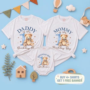 May include: Two white short-sleeve t-shirts and one white short-sleeve bodysuit. The shirts feature a blue number one, a brown teddy bear, and the text Daddy of the 1st Birthday Boy and Mommy of the 1st Birthday Boy. The bodysuit says Birthday Boy Jackson.
