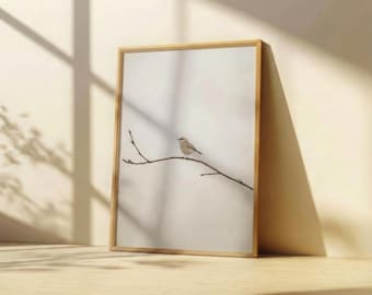 May include: A framed print featuring a small bird perched on a slender branch. The artwork is set against a soft, neutral background, with a natural wood frame. The image is leaning against a wall, with shadows from the sunlight.