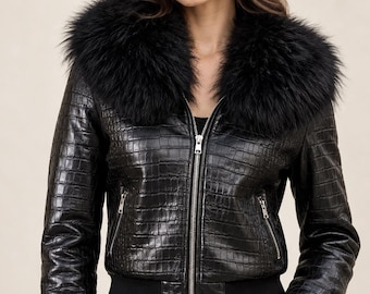 Könnte beinhalten: Eine schwarze Lederjacke mit Krokodilprägung, ausgestattet mit einem großen schwarzen Kunstfellkragen, einem silbernen Frontreißverschluss sowie schwarzen Rippbündchen an Ärmeln und Saum. Das Logo APPOLLO LEATHER ist oben links zu sehen.