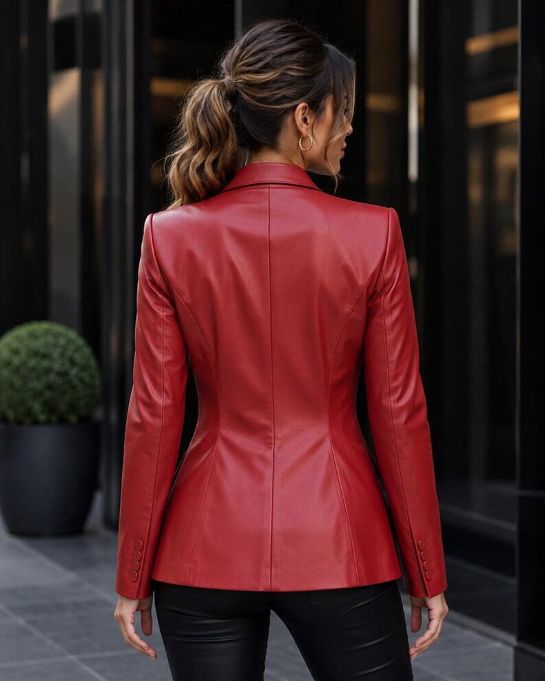 May include: A red leather blazer with a tailored fit. The blazer features a classic notched lapel, buttoned cuffs, and a structured silhouette. The back view shows the blazer's seams and design details. The model is wearing black pants.