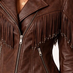 K&ouml;nnte beinhalten: Braune Lederjacke mit Fransen. Die Jacke hat einen Reverskragen, einen Rei&szlig;verschluss und mehrere Taschen. Die Fransen sind mit silberfarbenen Nieten verziert, was dem Kleidungsst&uuml;ck einen Hauch von Flair verleiht.