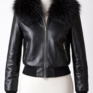 May include: Black leather bomber jacket with a black fur collar. The jacket features a zip-up front, two side pockets, and ribbed cuffs and hem. The jacket is displayed on a white mannequin.