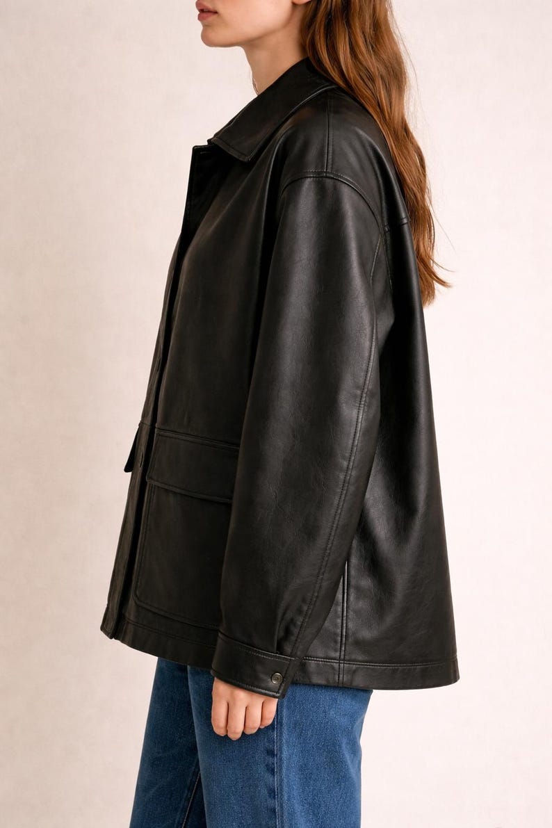 May include: Black faux leather jacket with a collared neckline, two front pockets, and buttoned cuffs. The jacket has a classic, slightly oversized fit, suitable for various outfits.