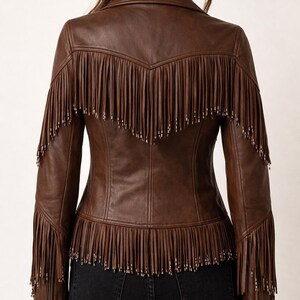 K&ouml;nnte beinhalten: Braune Lederjacke mit Fransen an R&uuml;cken, &Auml;rmeln und Saum. Die Jacke hat einen klassischen Kragen und eine taillierte Silhouette. Die Fransen sind mit kleinen silberfarbenen Nieten verziert. Ein stilvolles Oberbekleidungsst&uuml;ck.