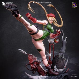 May include: A detailed figurine of a blonde character with long braided hair wearing a red beret, green leotard, and red gloves performing a high kick. The character stands on a base featuring a red fire hydrant, a manhole cover, and a cat.