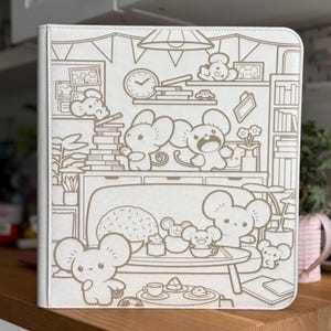 May include: A white binder featuring a brown line art illustration of a cosy room filled with cartoon mice. The scene depicts multiple mice interacting with furniture, books, a clock, and a table set with food, all rendered in a simple, clean style.