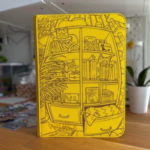 May include: A bright yellow binder featuring a black line art illustration of a bookshelf filled with books, potted plants, and various cat characters. The word vaultx is printed in small black letters at the bottom centre of the front cover.