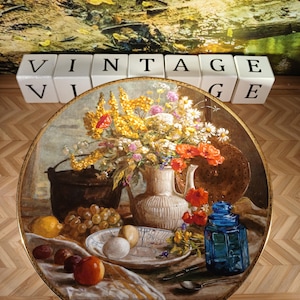 Può includere: Dipinto di natura morta vintage su un piatto decorativo. Il piatto presenta una composizione floreale, frutta e un barattolo di vetro blu. La parola "VINTAGE" è scritta con blocchi di lettere bianche.