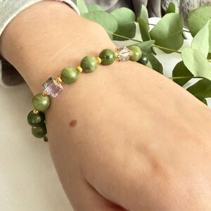 Könnte beinhalten: Ein grünes Perlenarmband mit goldenen Akzenten und einer klaren, facettierten Perle. Das Armband besteht aus runden, grünen Perlen und wird am Handgelenk getragen. Es ist ein Schmuckstück.