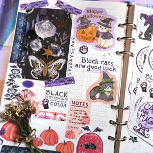 a beautiful halloween scrapbook journal spread of spooky halloween stickers, featuring moonchu's original art sticker sheet about black cats. features several black cat text, including black cats are good luck and i love black cats forever, as well as black cats with witch hats, paw prints, crystal ball, cat ghosts etc.
