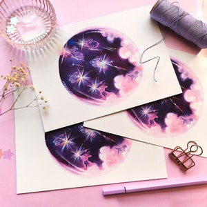 May include: Three prints of a watercolor painting depicting a purple and pink galaxy with white stars and shooting stars.  The galaxy is surrounded by white clouds and there are small white rabbits in the galaxy.