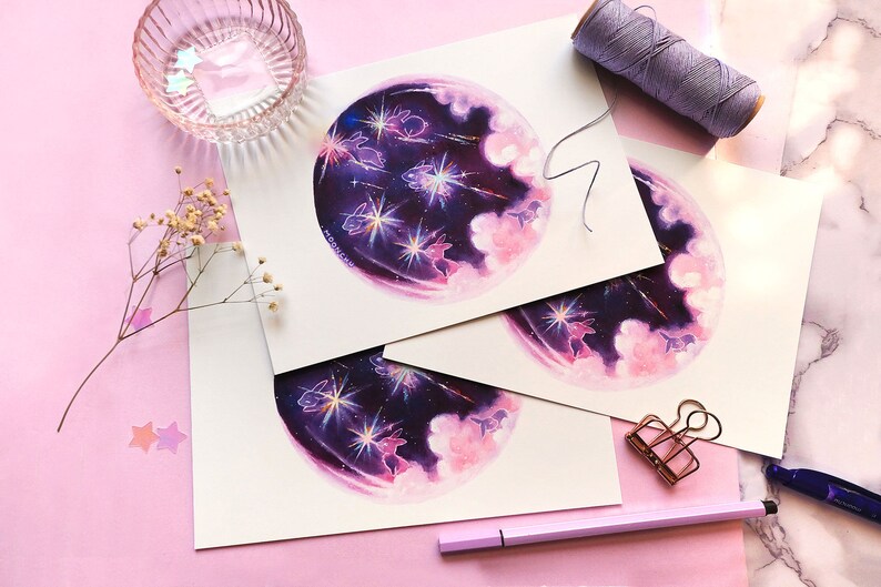 May include: Three prints of a watercolor painting depicting a purple and pink galaxy with white stars and shooting stars.  The galaxy is surrounded by white clouds and there are small white rabbits in the galaxy.