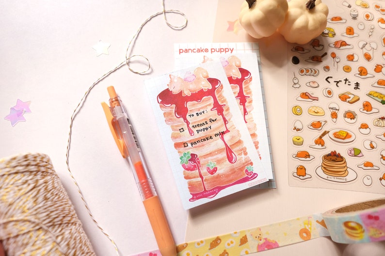 以下が含まれることがあります： 「To Buy!」と書かれたリストと、チェックボックスに「treats for puppy」と「pancake mix」と書かれた、漫画のパンケーキパピーが描かれたステッカーシートです。
