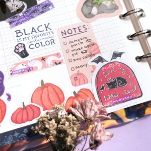 Puede incluir: Una colecci&oacute;n de pegatinas con tem&aacute;tica de Halloween que incluyen calabazas, fantasmas, un gato negro y una cita que dice "Me encanta mi peque&ntilde;o diablo". Las pegatinas est&aacute;n sobre un fondo blanco con un patr&oacute;n de cuadr&iacute;cula.