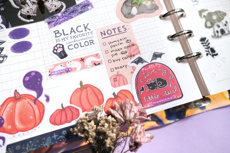 Puede incluir: Una colecci&oacute;n de pegatinas con tem&aacute;tica de Halloween que incluyen calabazas, fantasmas, un gato negro y una cita que dice "Me encanta mi peque&ntilde;o diablo". Las pegatinas est&aacute;n sobre un fondo blanco con un patr&oacute;n de cuadr&iacute;cula.