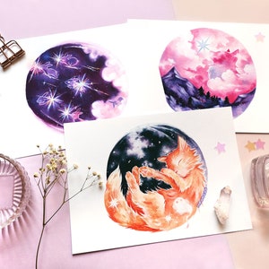 May include: Three watercolor paintings on white paper with a pink background. The first painting depicts a purple and pink night sky with white clouds and shooting stars. The second painting shows a pink and purple sunset with a mountain range in the background. The third painting features a sleeping orange cat with a starry night sky in the background.