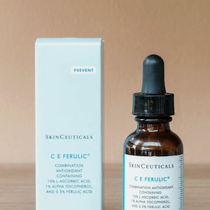 May include: A skincare product set featuring a brown glass bottle with a black dropper and a light blue box. Both items display the "SkinCeuticals C E Ferulic" label, with text detailing ingredients and the word "PREVENT". The bottle and box each contain 30 ml / 1 fl oz.