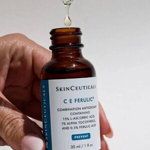 May include: A brown glass bottle of SkinCeuticals C E Ferulic serum with a dropper dispensing the product. The label indicates the serum contains 15% L-Ascorbic Acid, 1% Alpha Tocopherol, and 0.5% Ferulic Acid. The bottle contains 1 fl oz of serum.