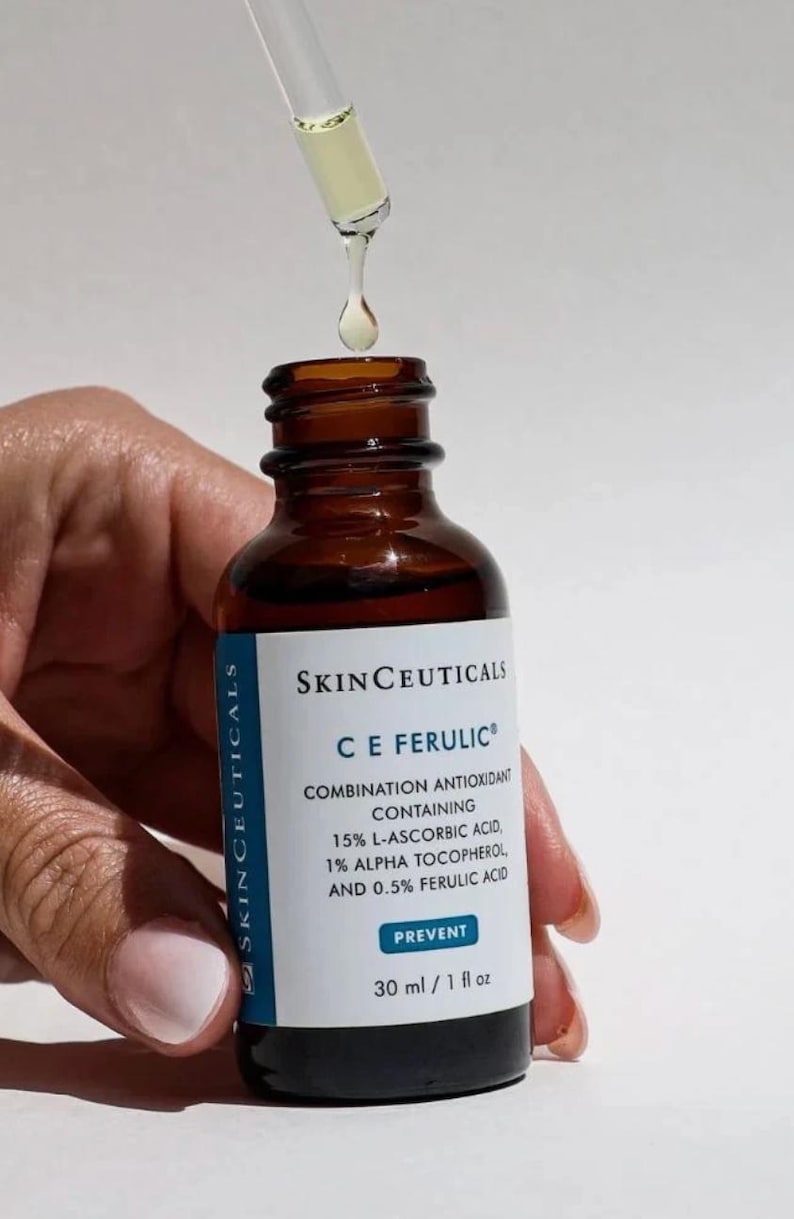 May include: A brown glass bottle of SkinCeuticals C E Ferulic serum with a dropper dispensing the product. The label indicates the serum contains 15% L-Ascorbic Acid, 1% Alpha Tocopherol, and 0.5% Ferulic Acid. The bottle contains 1 fl oz of serum.