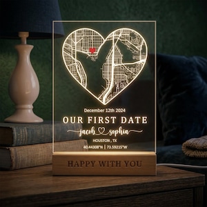 May include: A lighted acrylic sign with a heart-shaped map design. The sign displays the text "OUR FIRST DATE" with names and a date. The base is made of wood, and the text "HAPPY WITH YOU" is engraved on it. The sign is illuminated.