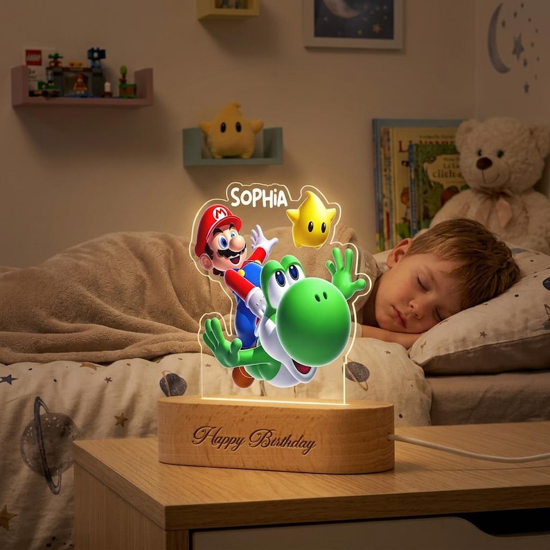 May include: An illuminated acrylic night light featuring a colourful graphic of Mario riding Yoshi with a yellow star and the name SOPHIA printed above. The light is mounted on a light-coloured wooden base with the text Happy Birthday engraved on the front.