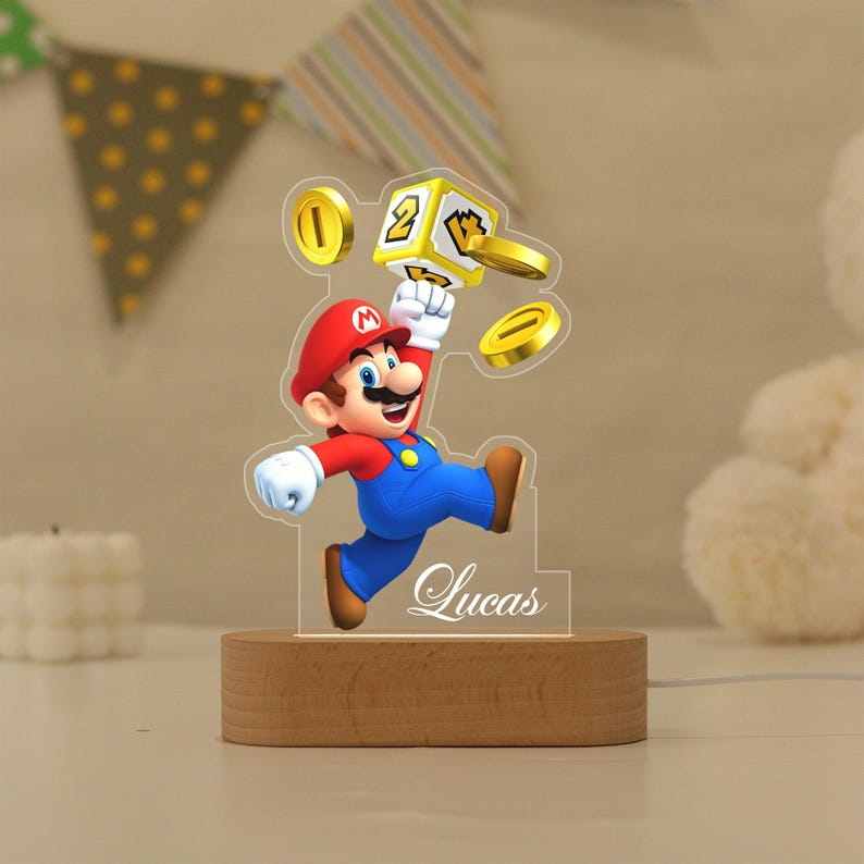 May include: A custom acrylic night light featuring a colourful graphic of Mario jumping towards a yellow question block and gold coins. The clear acrylic panel is personalised with the name Lucas in white script and sits on a light wood base.