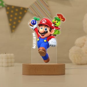 May include: A custom acrylic night light featuring a colourful graphic of Mario holding a blue orb with a green sprout, accompanied by a green character with a red crown. The name William is printed vertically in white text on the clear acrylic panel.