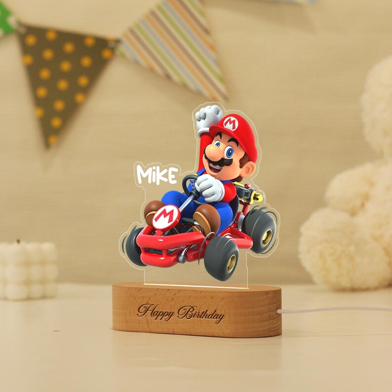 May include: A custom acrylic night light featuring a colourful graphic of Mario driving a red go-kart with the name Mike printed above. The clear acrylic cutout is mounted on a light-coloured wooden base engraved with the text Happy Birthday.