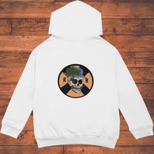 Op de afbeelding: Witte hoodie met een cirkelvormige afbeelding op de rug. De afbeelding toont een schedel met een blauwe pet en een boom die eruit groeit, in een zwarte en oranje cirkel. De letters "R" staan aan weerszijden van de cirkel.