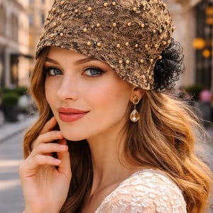 Puede incluir: Un sombrero cloche de encaje marrón adornado con pequeñas perlas y una flor de tela negra. El sombrero se usa con pendientes dorados y una blusa de encaje color crema. La imagen está ambientada al aire libre con un fondo borroso.