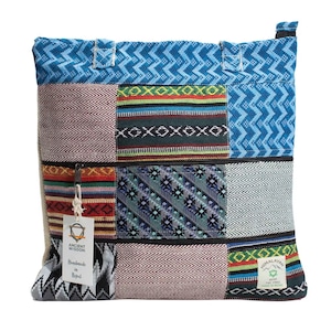 Könnte beinhalten: Eine quadratische Tragetasche mit einem Patchwork-Design aus verschiedenen gewebten Stoffen in Blau, Rot, Grün und Schwarz. Die Tasche hat einen Reißverschluss oben, zwei Griffe und zwei weiße Etiketten mit Text, darunter Ancient Wisdom und Himalayan Hemp.